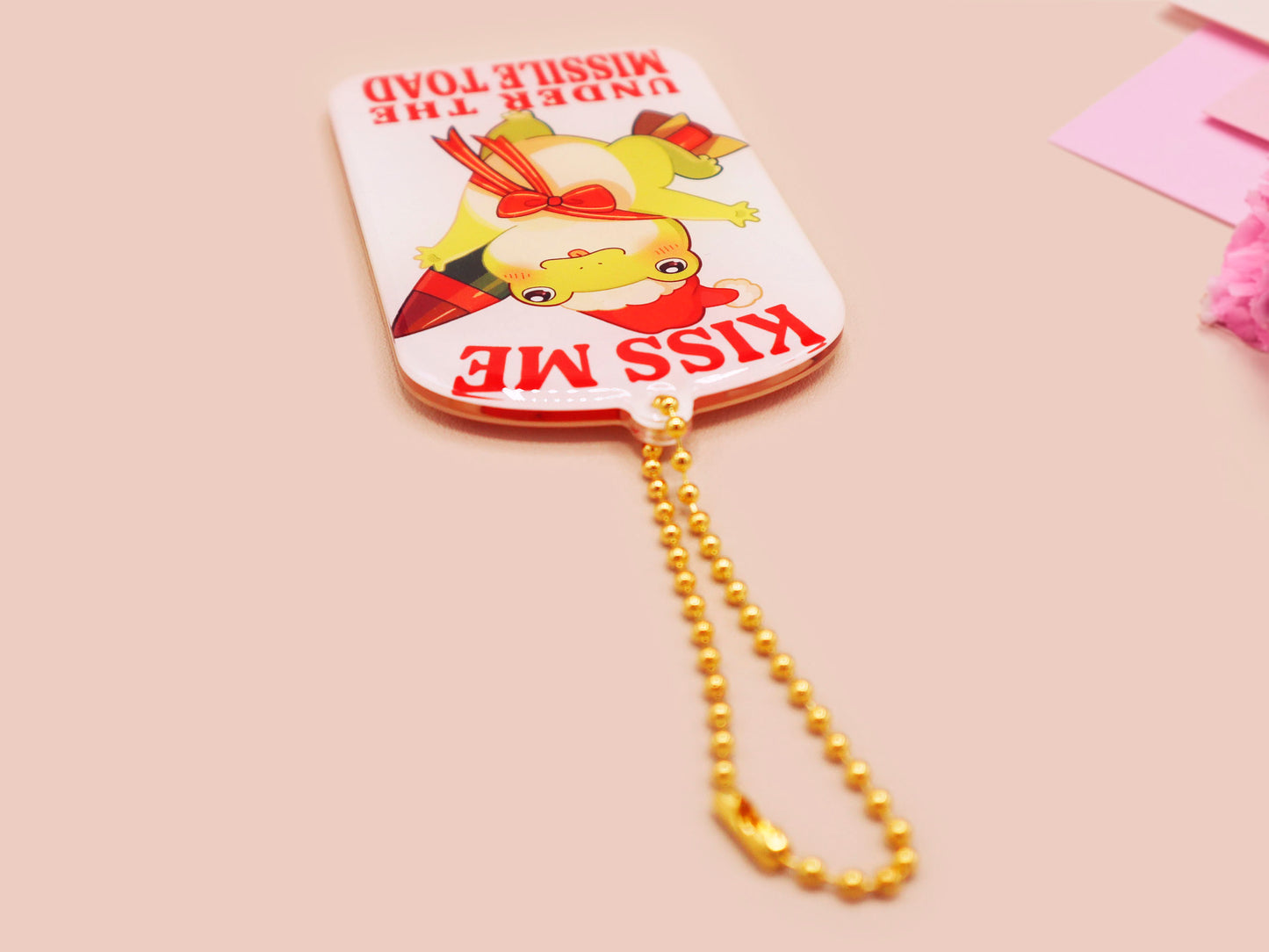 Acrylic epoxy christmas tree hanging decoration with a large acrylic charm of a cute chibi santa frog with a missile tied to its back with a red ribbon with the quote kiss me under the missile toad