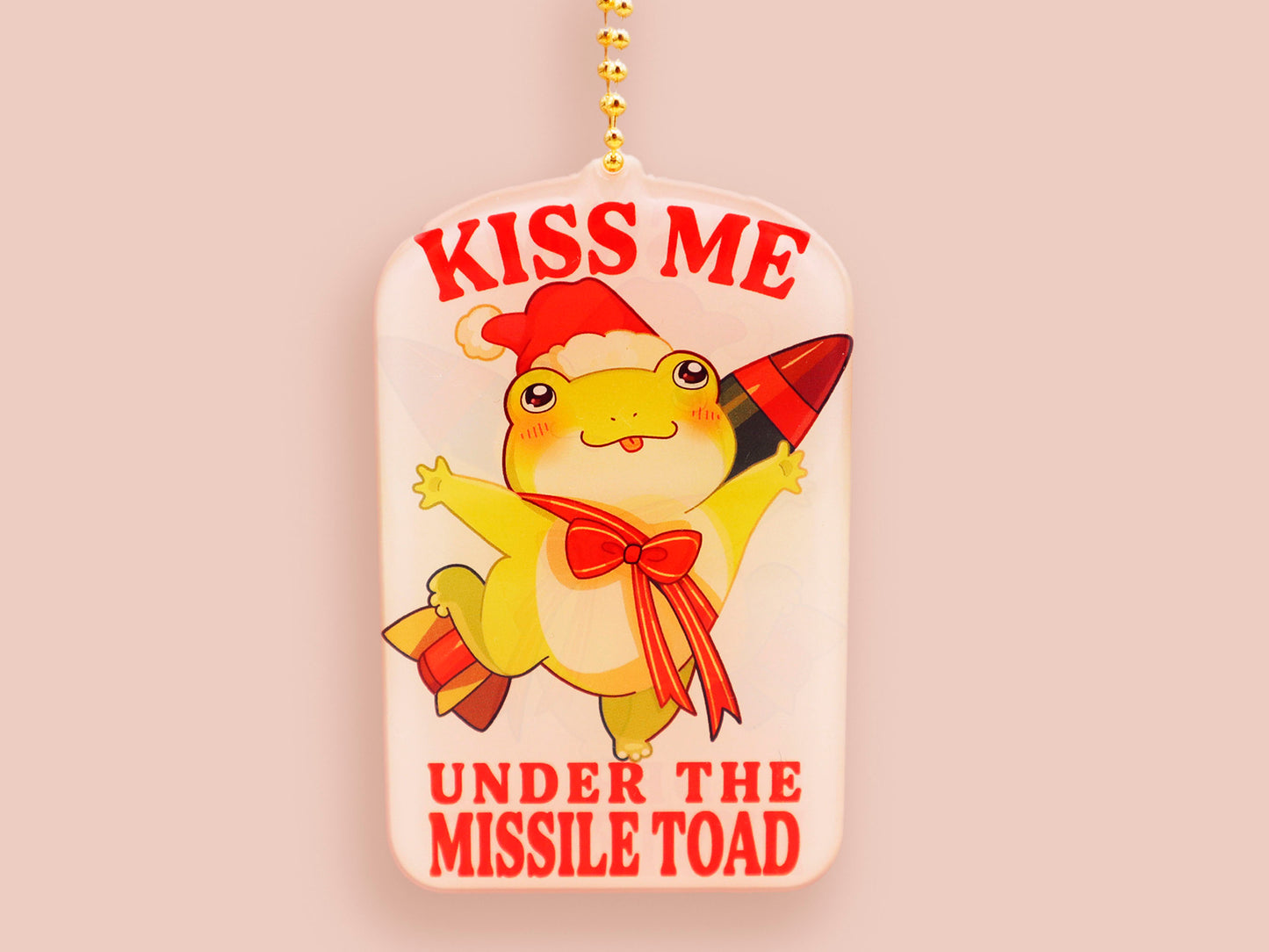 Acrylic epoxy christmas tree hanging decoration with a large acrylic charm of a cute chibi santa frog with a missile tied to its back with a red ribbon with the quote kiss me under the missile toad