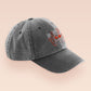 A vintage dark grey baseball cap hat with an embroidered cute chibi Mothman crytid with the quote Live Lamp Lurk.