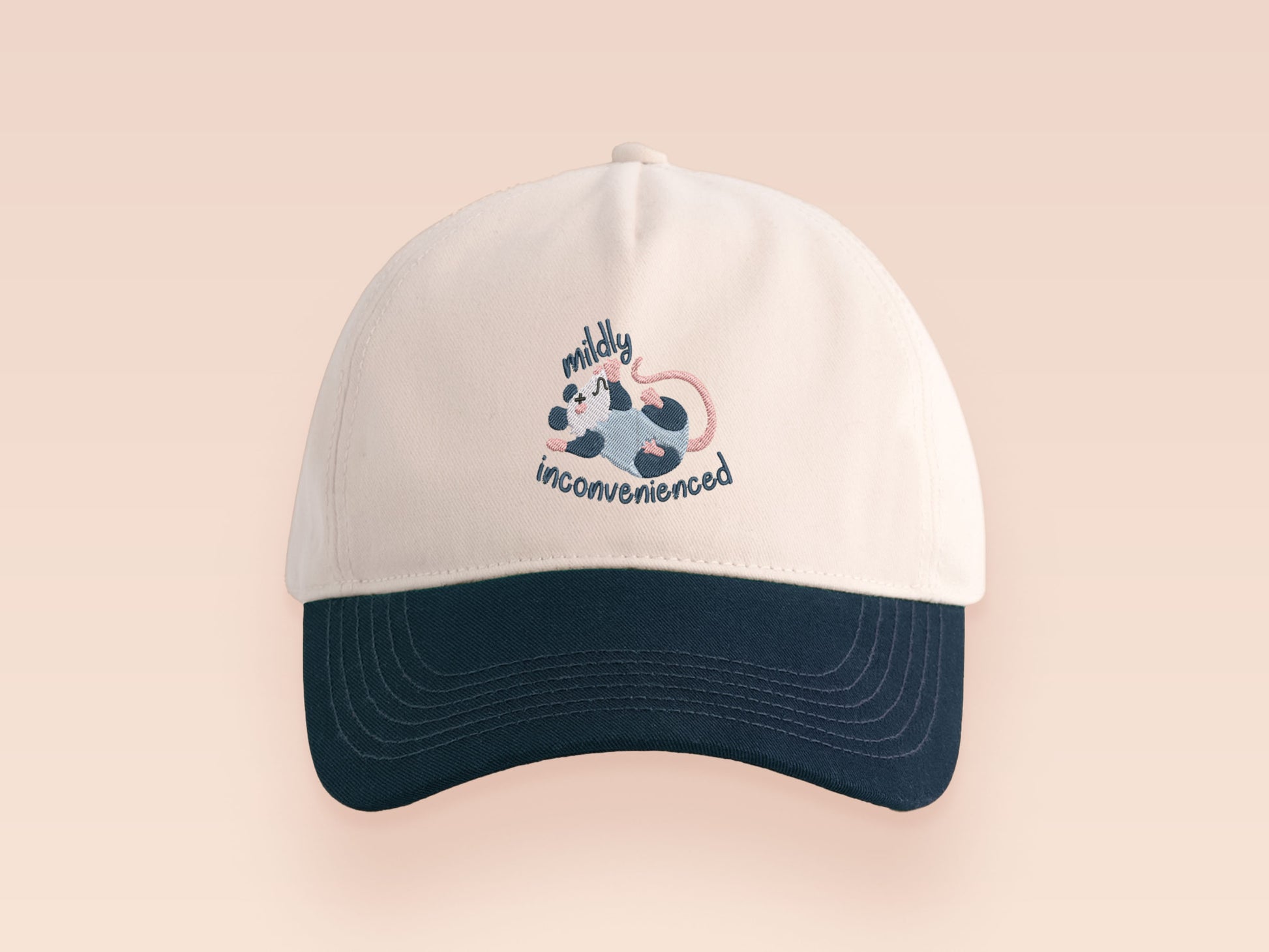 Vintage style truckers baseball cap with a contrast cream and navy peak design with an embroidered possum playing dead and the quote mildly inconveninced 