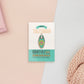 Gold Enamel Talisman Charm the words Mini Talisman sits on a long white and green backing card with gold accents. The backing card has details the symbolism of the different design elements of the Talisman pin.