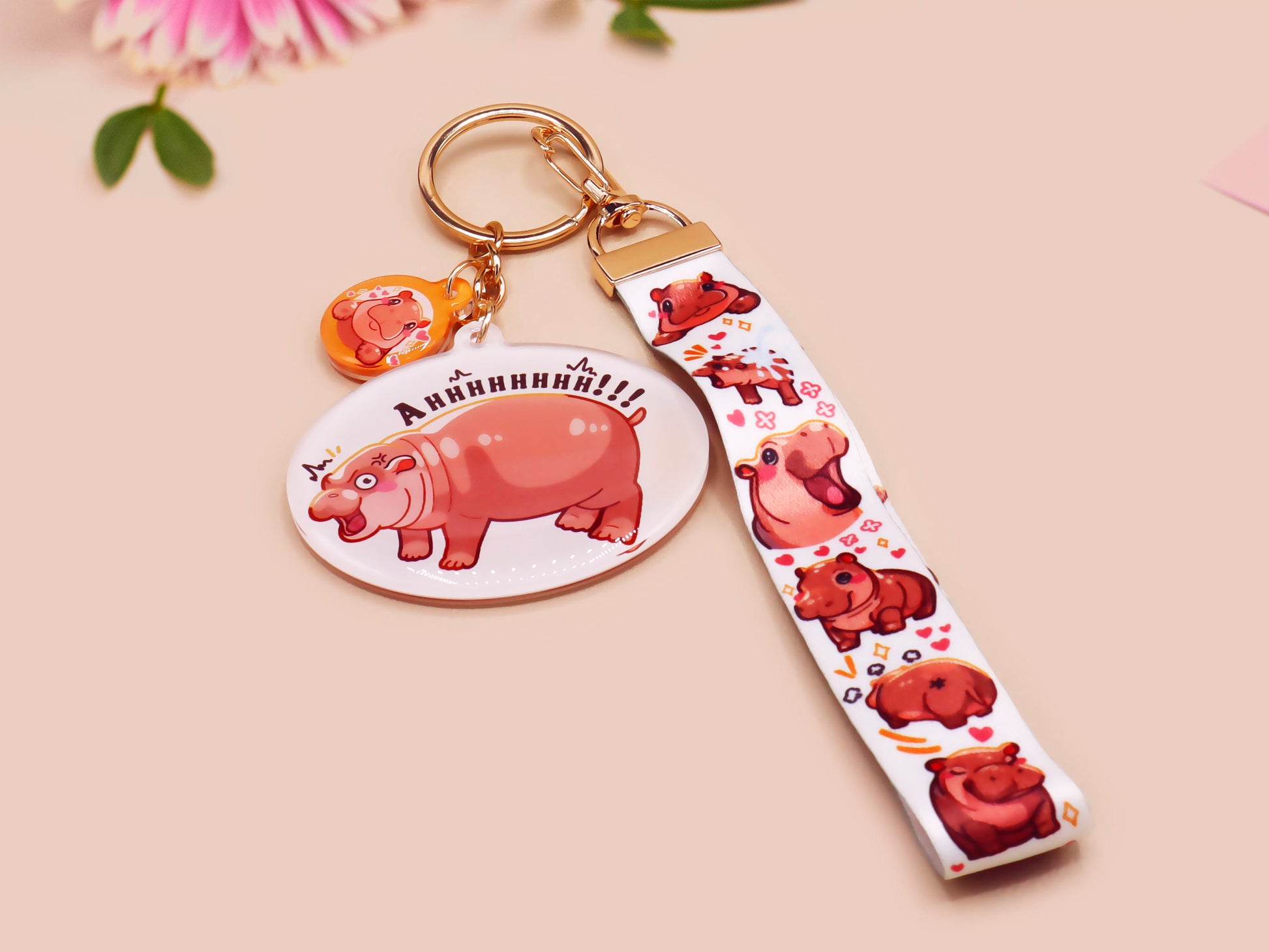 Acrylic keychain with a large charm of the fat angry pygmy hippo being picked up, a smaller charm of a cute baby hippo with the name Moo Deng in Thai and a matching mini lanyard of the pygmy hippo in multiple cute poses and expressions.