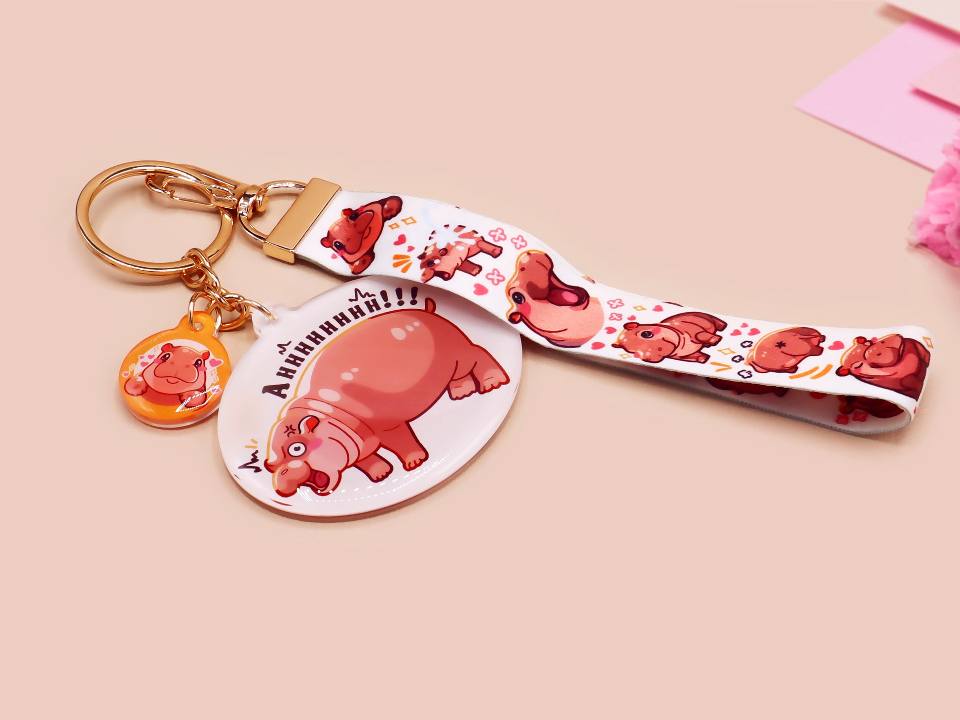 Acrylic keychain with a large charm of the fat angry pygmy hippo being picked up, a smaller charm of a cute baby hippo with the name Moo Deng in Thai and a matching mini lanyard of the pygmy hippo in multiple cute poses and expressions.