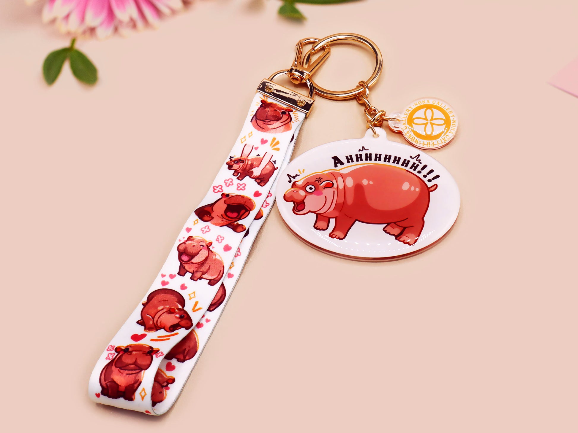 Acrylic keychain with a large charm of the fat angry pygmy hippo being picked up, a smaller charm of a cute baby hippo with the name Moo Deng in Thai and a matching mini lanyard of the pygmy hippo in multiple cute poses and expressions.