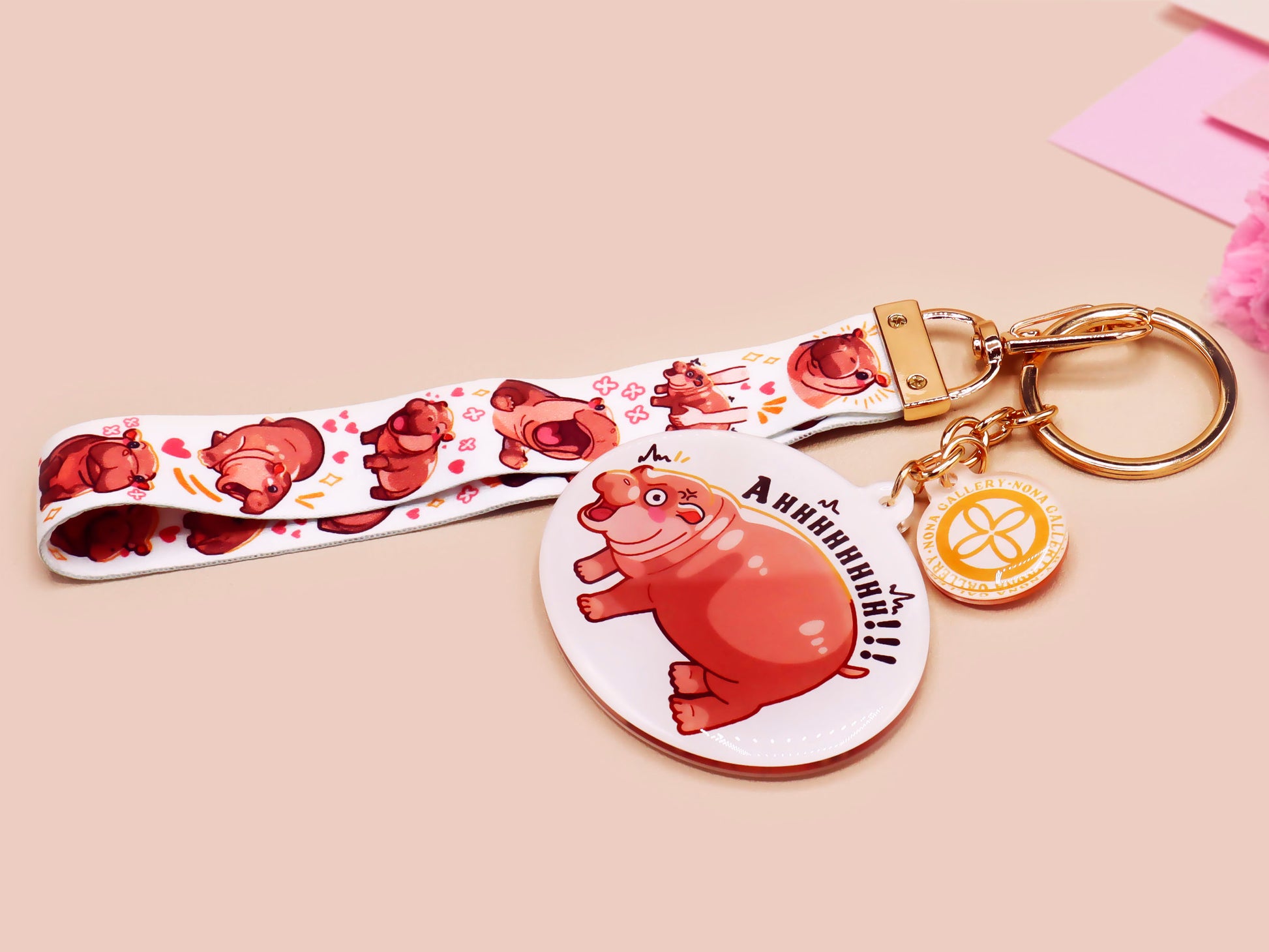 Acrylic keychain with a large charm of the fat angry pygmy hippo being picked up, a smaller charm of a cute baby hippo with the name Moo Deng in Thai and a matching mini lanyard of the pygmy hippo in multiple cute poses and expressions.
