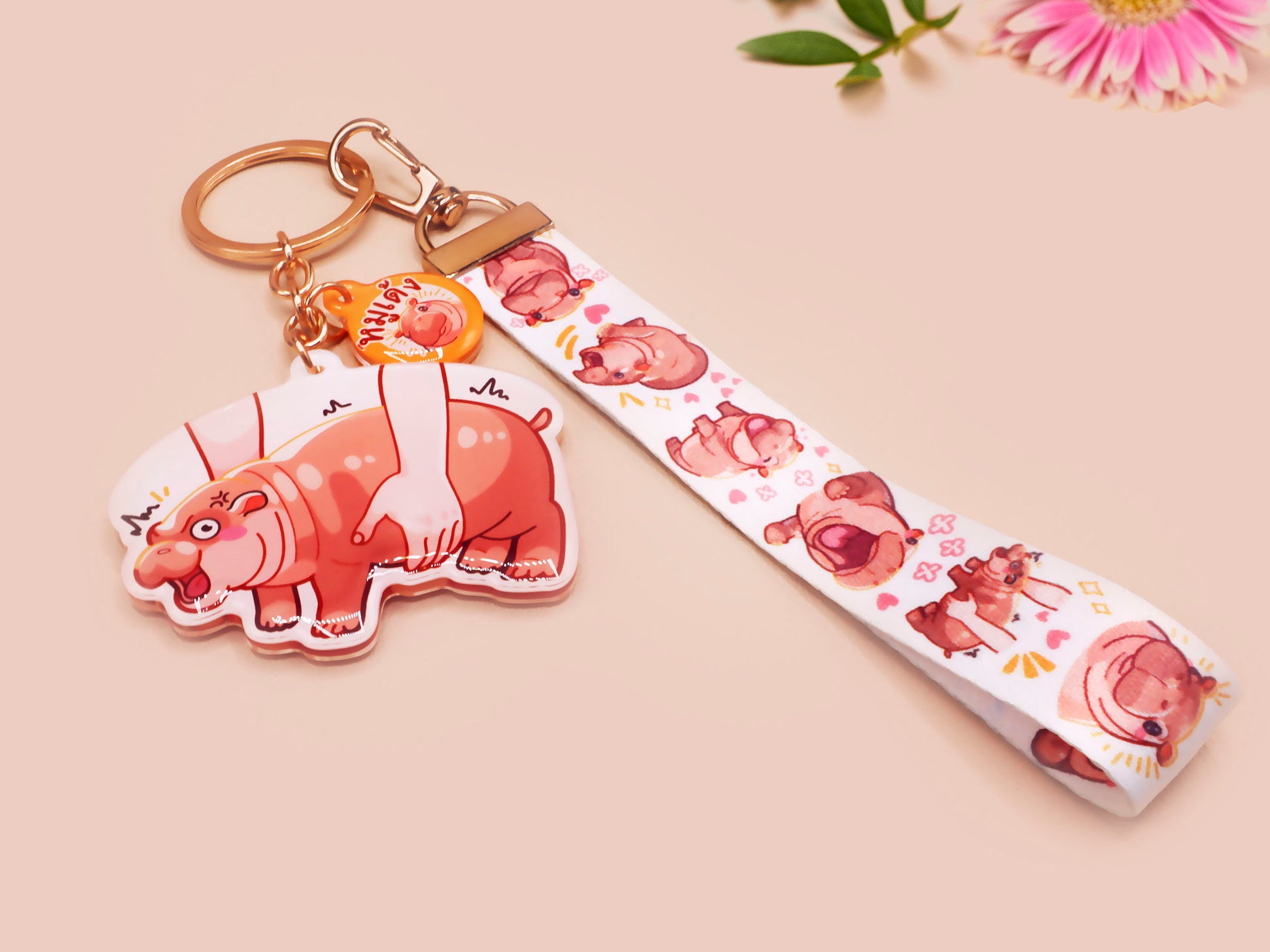 Acrylic keychain with a large charm of the fat angry pygmy hippo being picked up, a smaller charm of a cute baby hippo with the name Moo Deng in Thai and a matching mini lanyard of the pygmy hippo in multiple cute poses and expressions. 