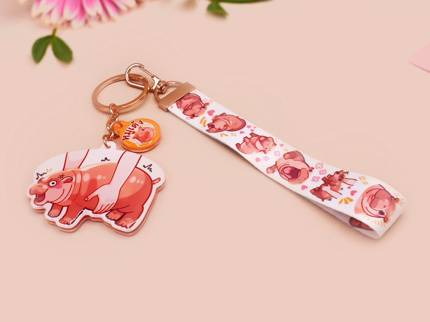 Acrylic keychain with a large charm of the fat angry pygmy hippo being picked up, a smaller charm of a cute baby hippo with the name Moo Deng in Thai and a matching mini lanyard of the pygmy hippo in multiple cute poses and expressions. 