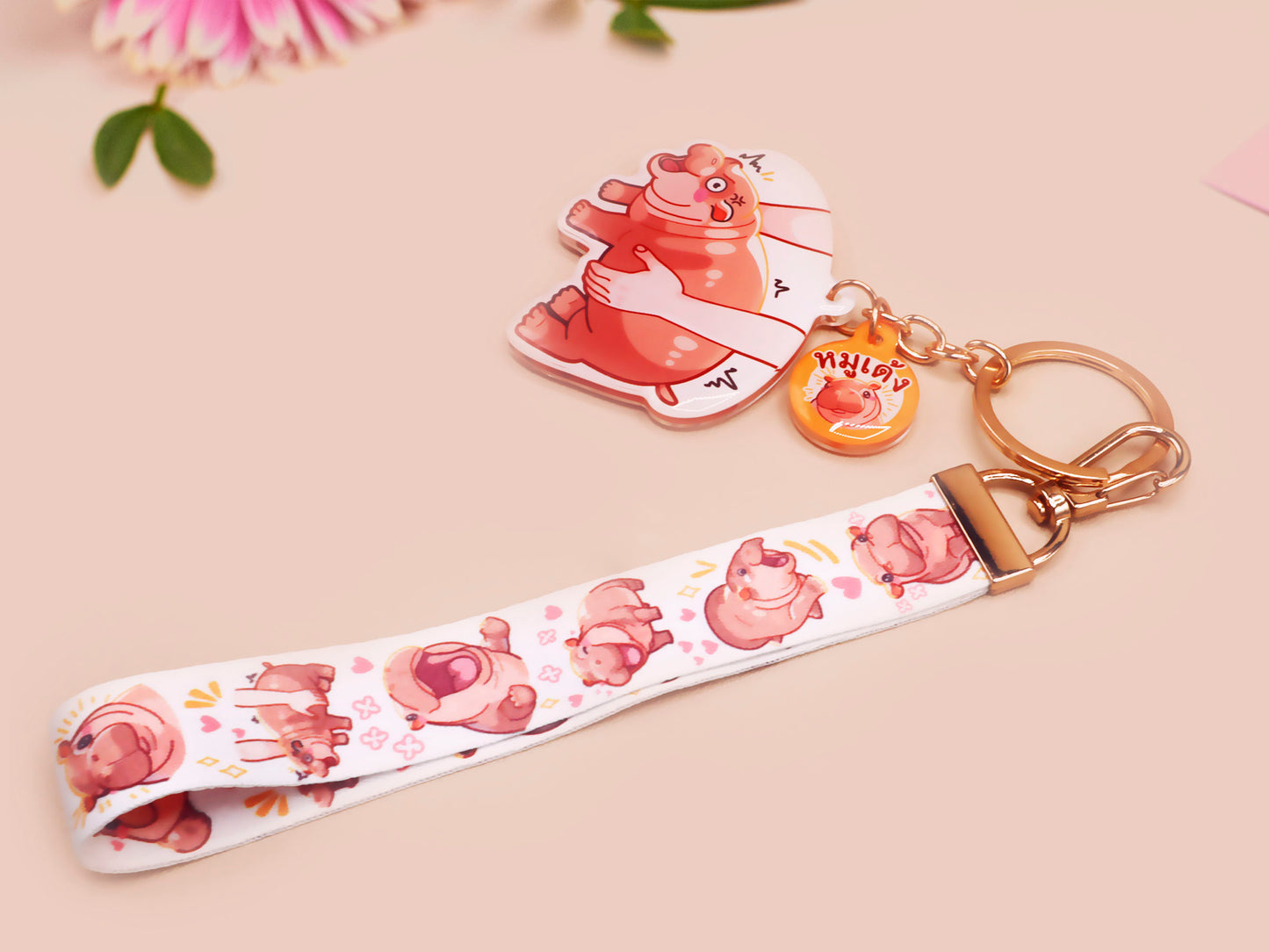 Acrylic keychain with a large charm of the fat angry pygmy hippo being picked up, a smaller charm of a cute baby hippo with the name Moo Deng in Thai and a matching mini lanyard of the pygmy hippo in multiple cute poses and expressions. 