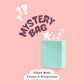 A pastel blue paper bag open with cartoon stars falling out of it, surrounded by the words Mystery Bag Filled With Treats & Surprises 