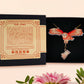 Mixed material handmade necklace of chibi cartoon flying barn owl with pearlescent wings carrying a removeable spell book charm, with a gold chain and black gift box with a yellow familiars collection gift sleeve.
