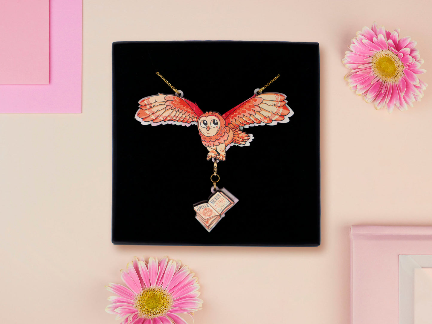 Mixed material handmade necklace of chibi cartoon flying barn owl with pearlescent wings carrying a removeable spell book charm, with a gold chain and black gift box.