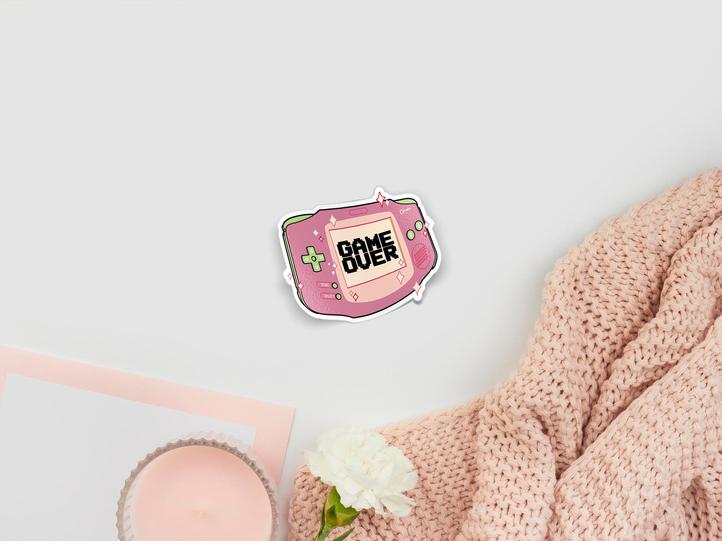Large sticker of digital illustration cartoons of cute pastel pink nintendo nes handheld console surrounded by sparkles, with the screen text game over