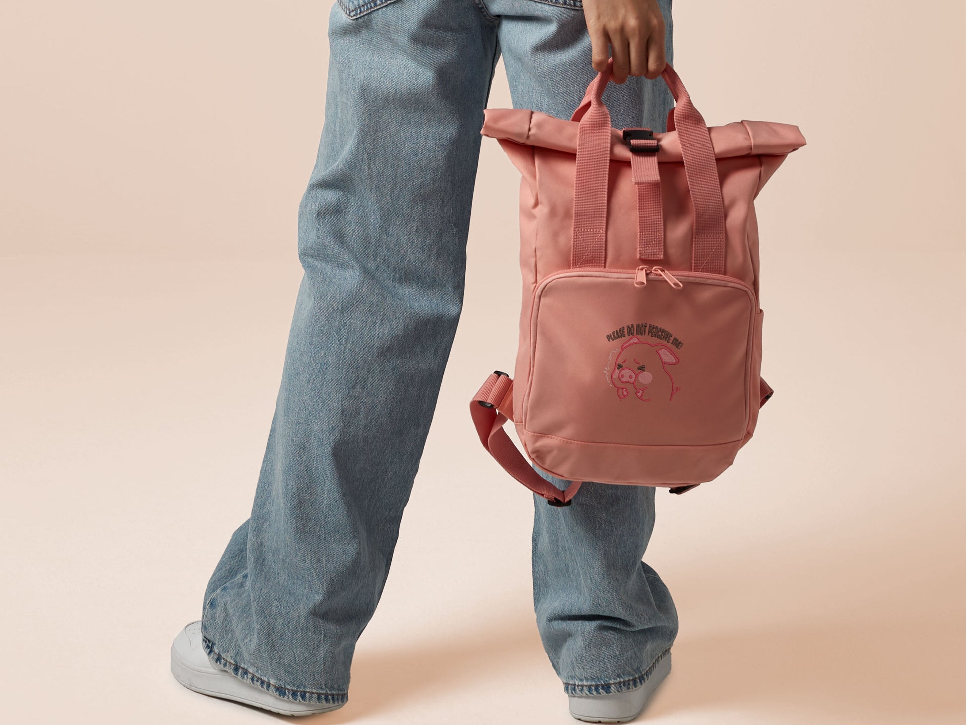 Pink roll top twin handle backpack with an embroided design of cute crying pig and the quote please do not percive me