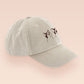 A cream baseball cap hat with an embroidered cute brown Popcat meme cat design.