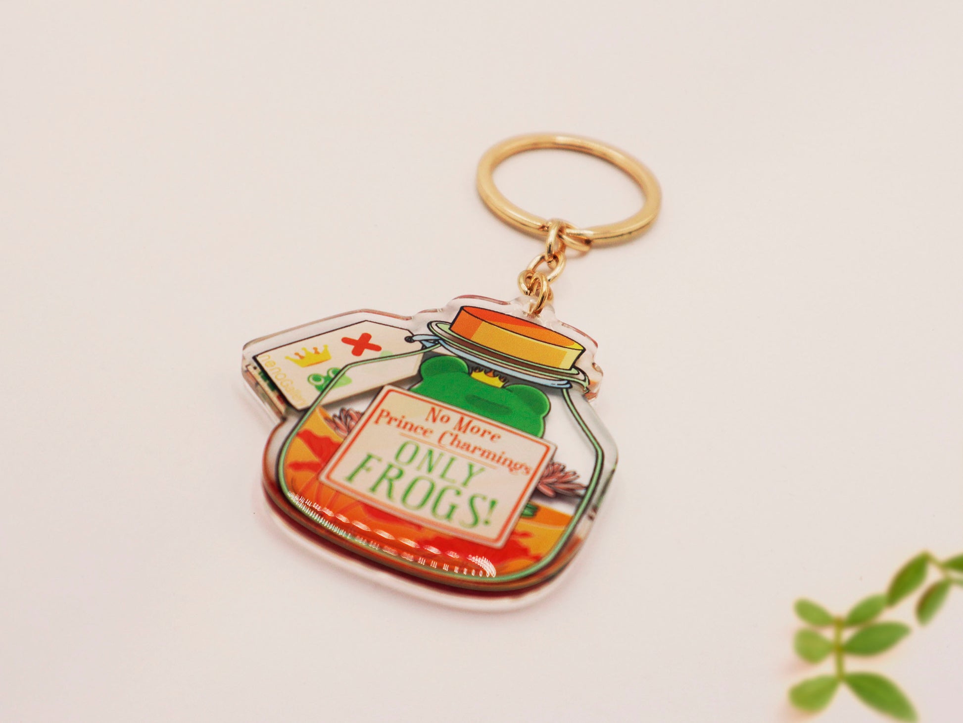Double sided epoxy keychain with golden clasp of a frog inside a potion bottle looking glum wearing a small crown and sat on a lily pad., with the potion bottle labelled Frog Transformation Potion