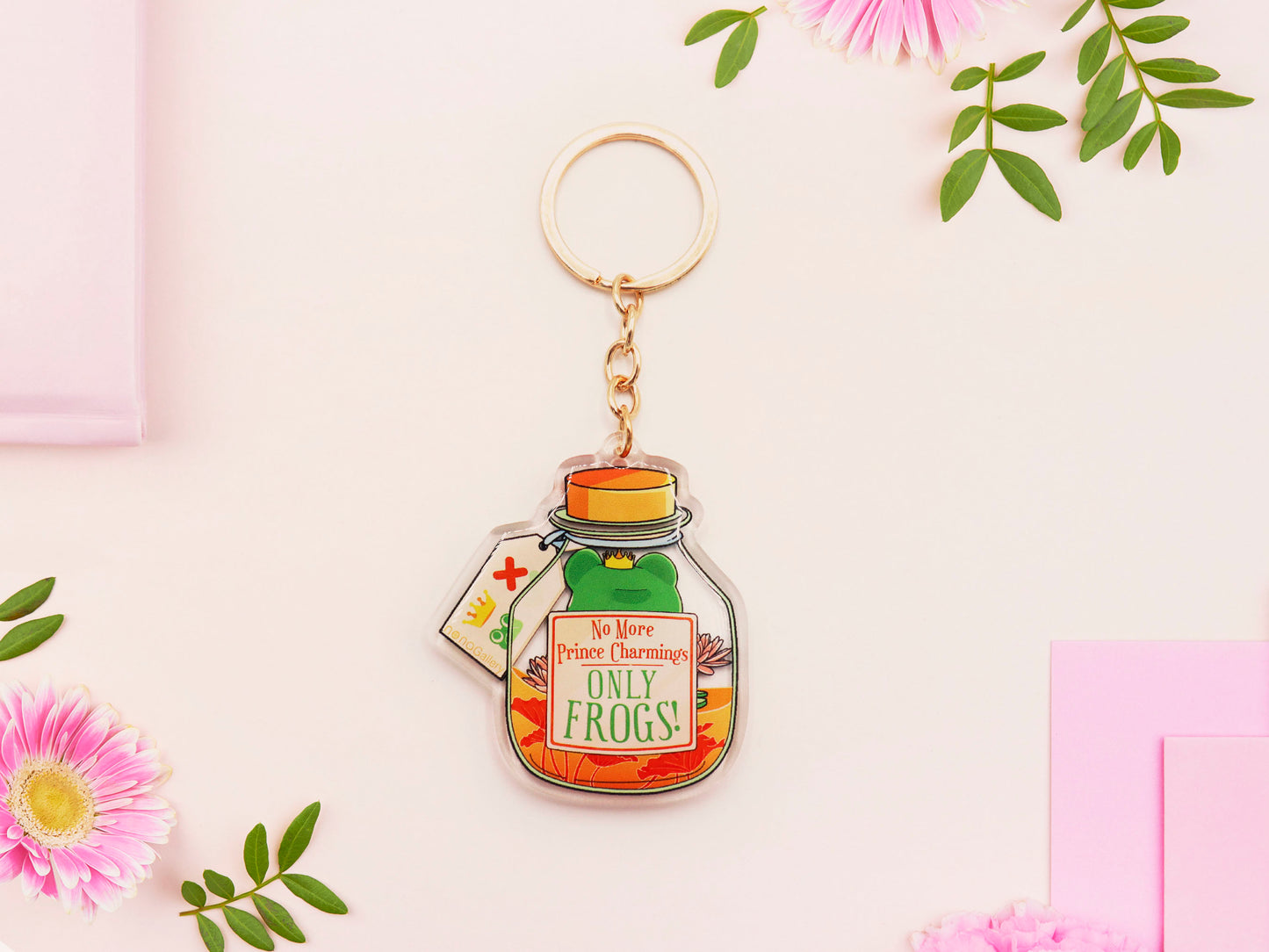 Double sided epoxy keychain with golden clasp of a frog inside a potion bottle looking glum wearing a small crown and sat on a lily pad., with the potion bottle labelled Frog Transformation Potion