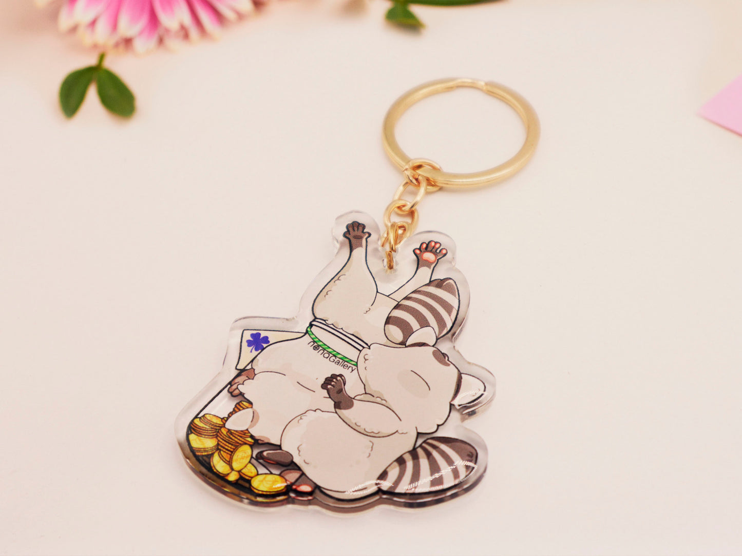 The back of a clear acrylic keychain with gold chain clasp of two cheeky raccoons stealing gold coins from inside a potion bottle labelled potion of good fortune