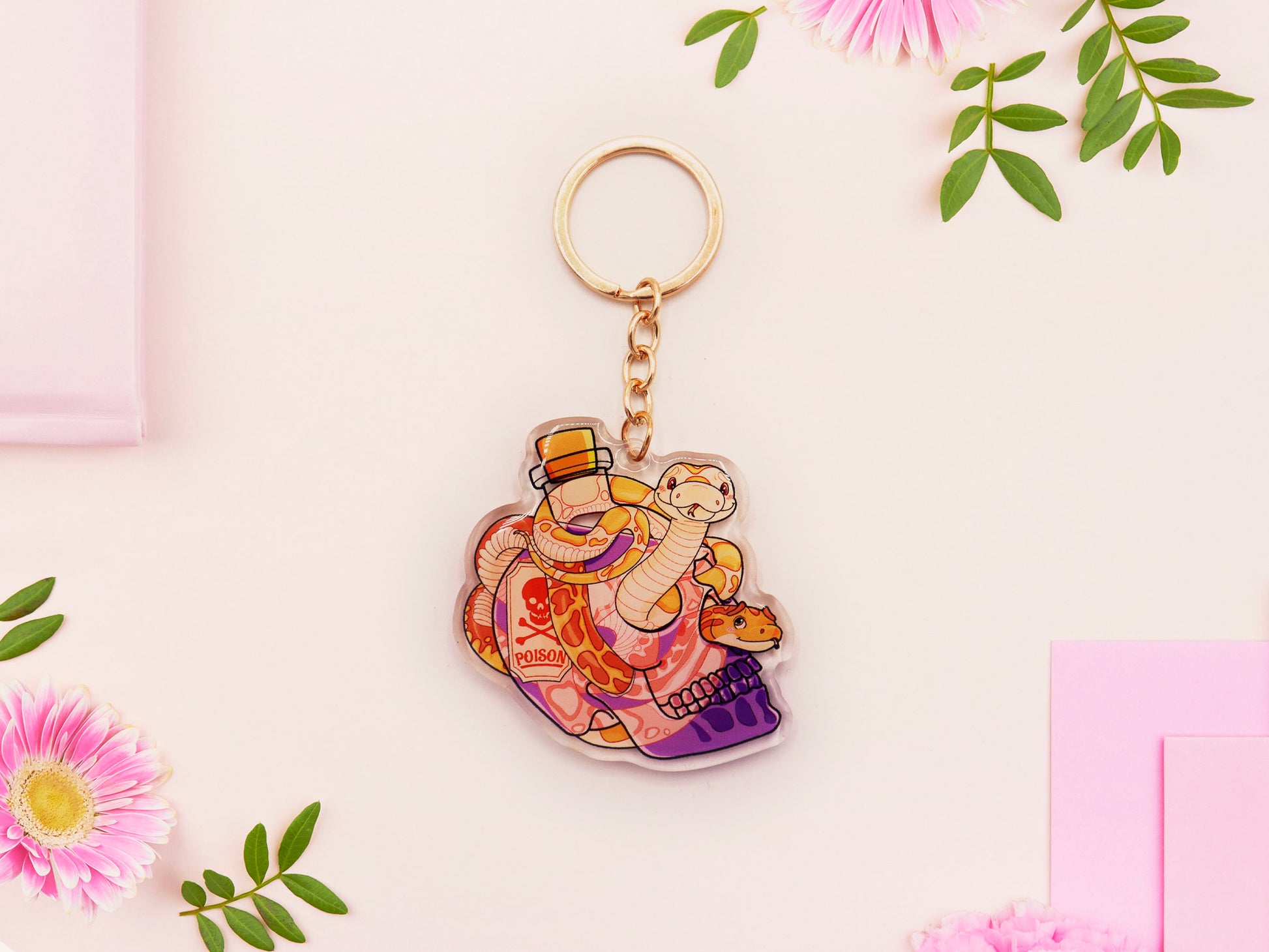 Clear acrylic double sided keyring with a cute cartoon illustrated skull shaped potion bottle with two yellow and brown corn snakes, filled with a purple liquid labelled with a skull and bones and the word poison.