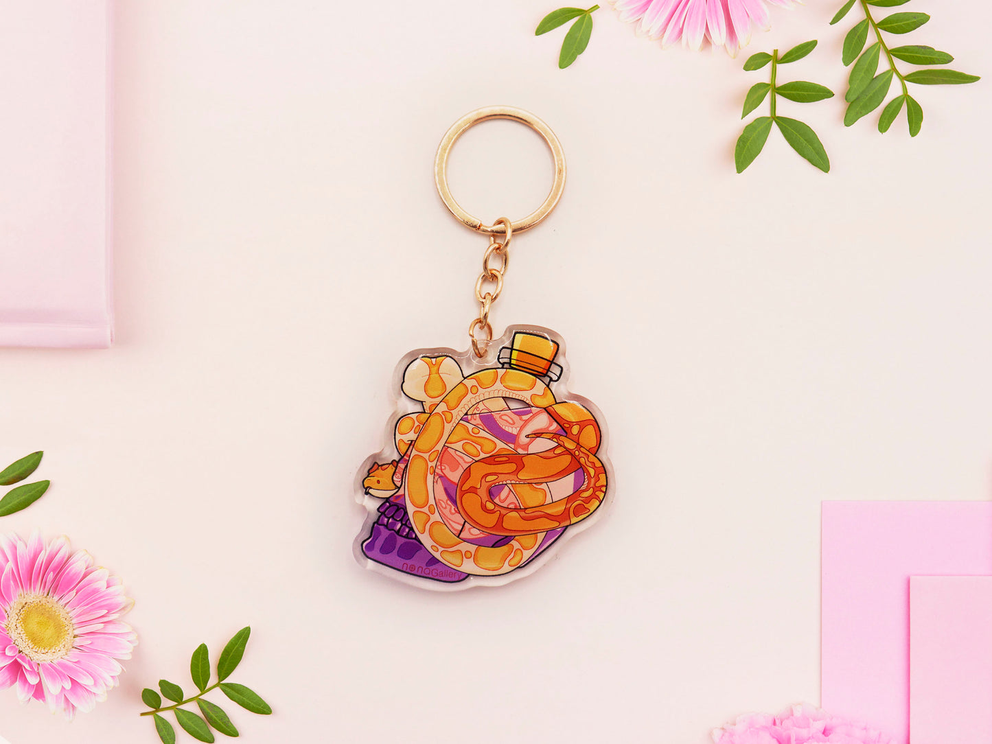 Clear acrylic double sided keyring with a cute cartoon illustrated skull shaped potion bottle with two yellow and brown corn snakes, filled with a purple liquid labelled with a skull and bones and the word poison.