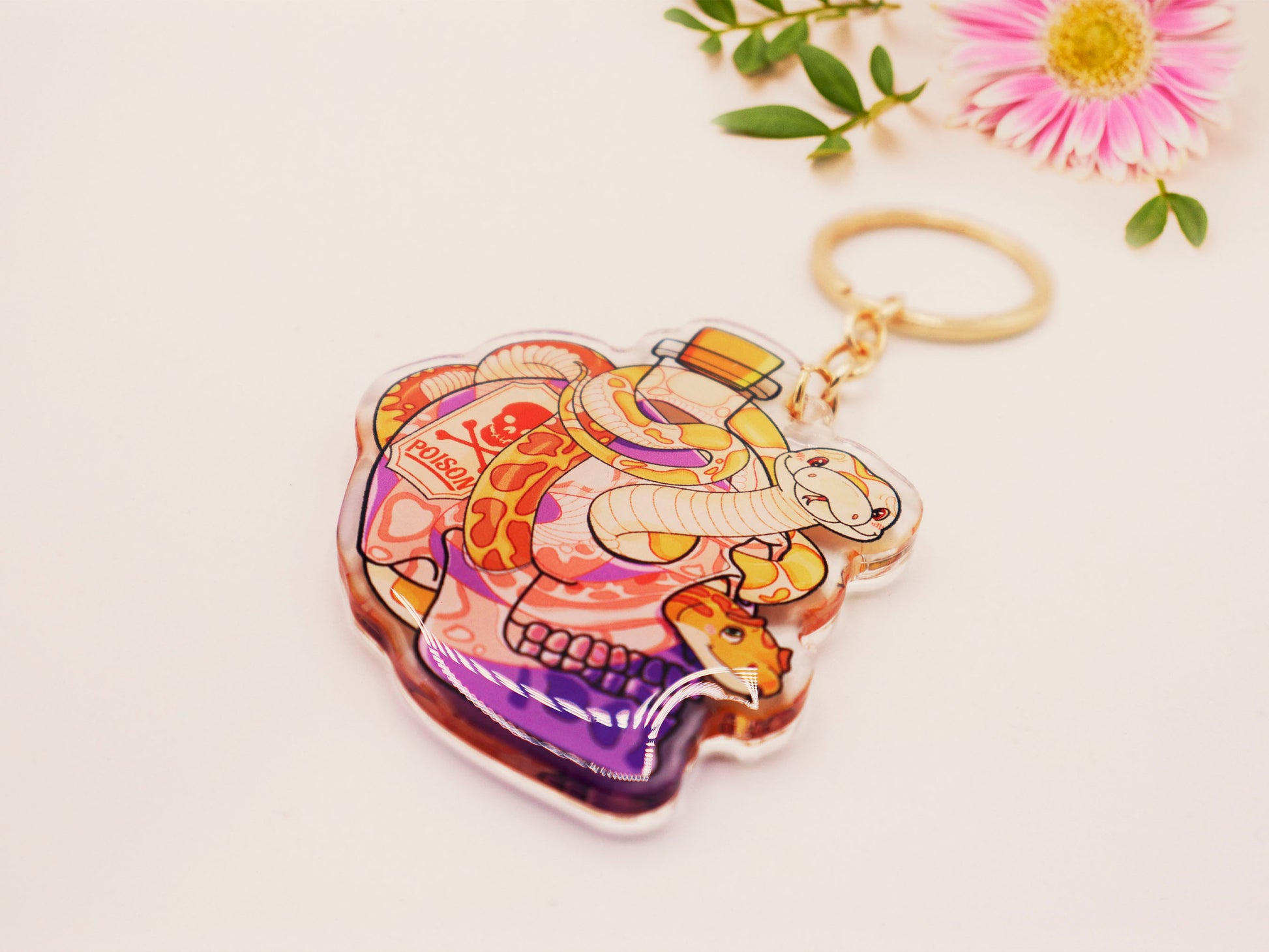 Clear acrylic double sided keyring with a cute cartoon illustrated skull shaped potion bottle with two yellow and brown corn snakes, filled with a purple liquid labelled with a skull and bones and the word poison.
