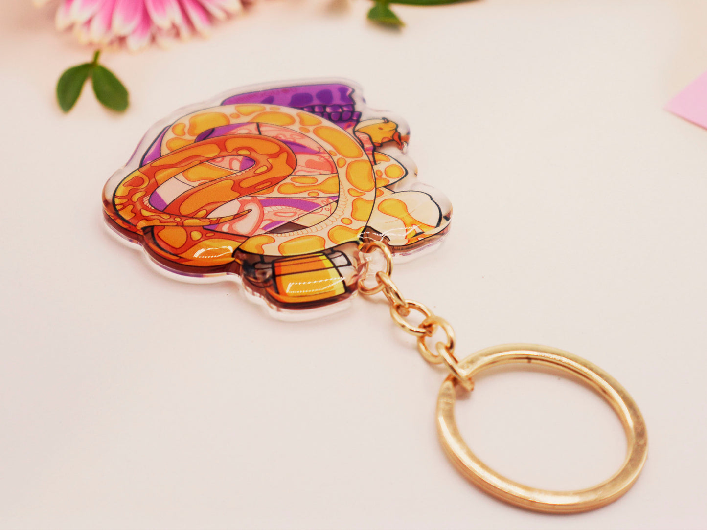 Clear acrylic double sided keyring with a cute cartoon illustrated skull shaped potion bottle with two yellow and brown corn snakes, filled with a purple liquid labelled with a skull and bones and the word poison.