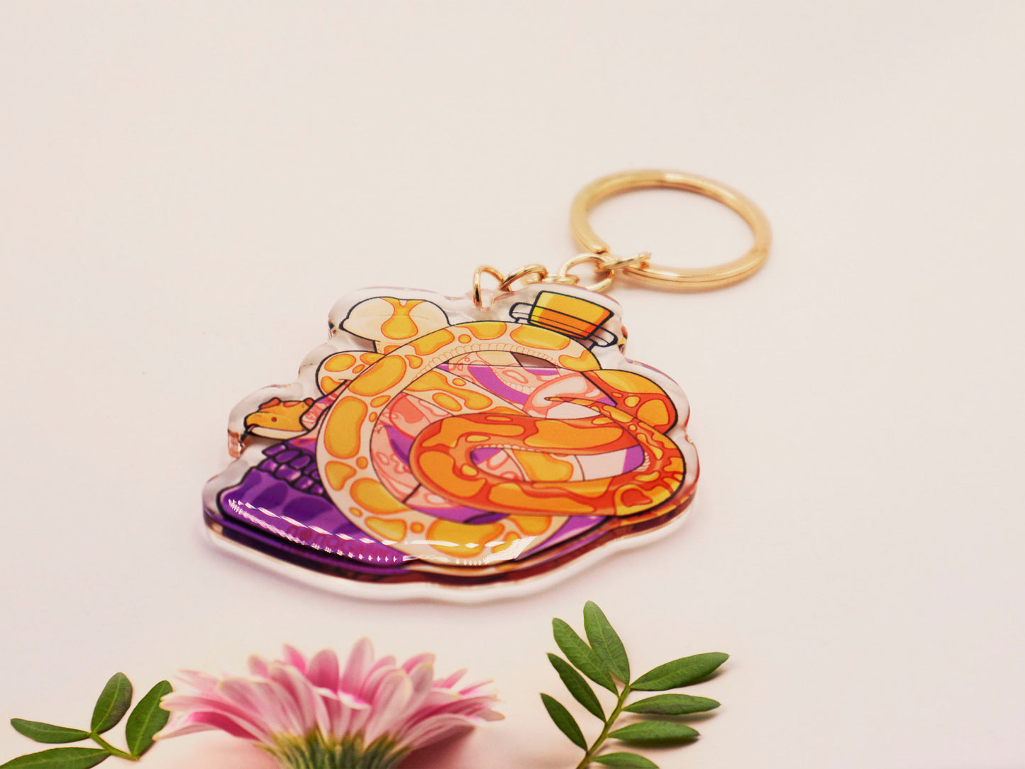 Clear acrylic double sided keyring with a cute cartoon illustrated skull shaped potion bottle with two yellow and brown corn snakes, filled with a purple liquid labelled with a skull and bones and the word poison.