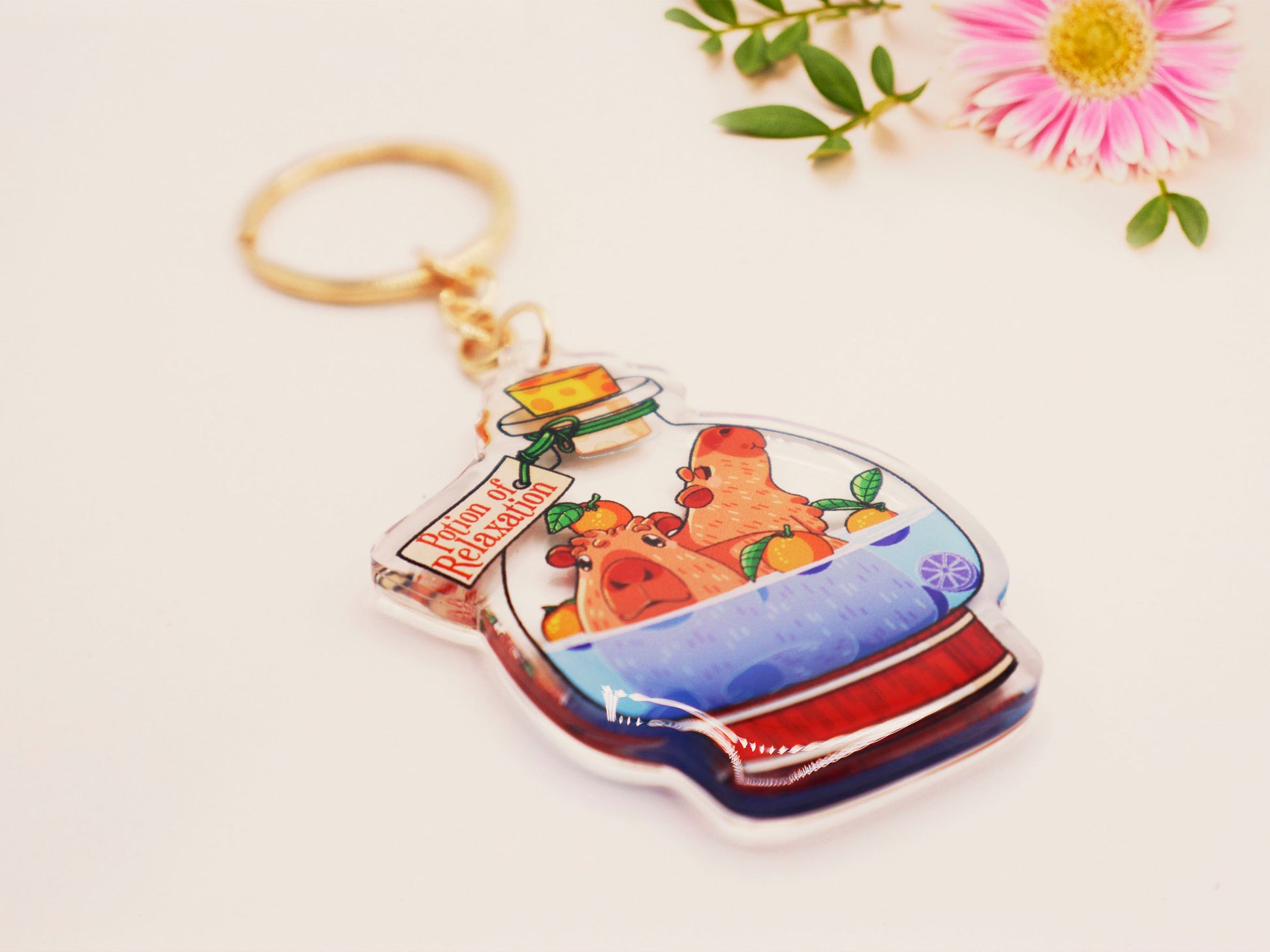 Double sided epoxy clear acrylic keychain with golden clasp of two happy capybaras sat inside an Onsen shaped potion bottle with yuzu oranges, with the potion bottle labelled Potion of Relaxation 