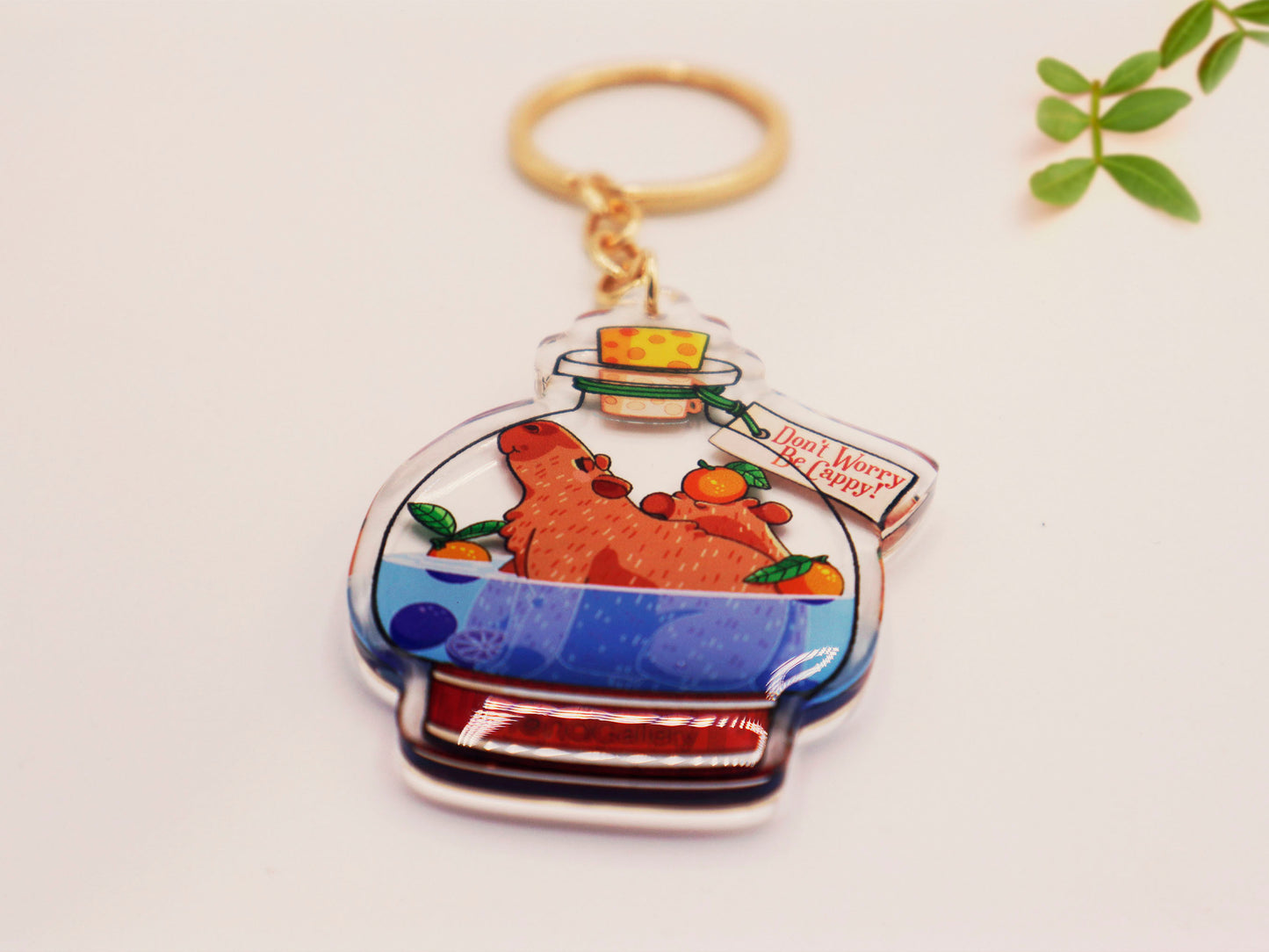 Double sided epoxy clear acrylic keychain with golden clasp of two happy capybaras sat inside an Onsen shaped potion bottle with yuzu oranges, with the potion bottle labelled Potion of Relaxation 