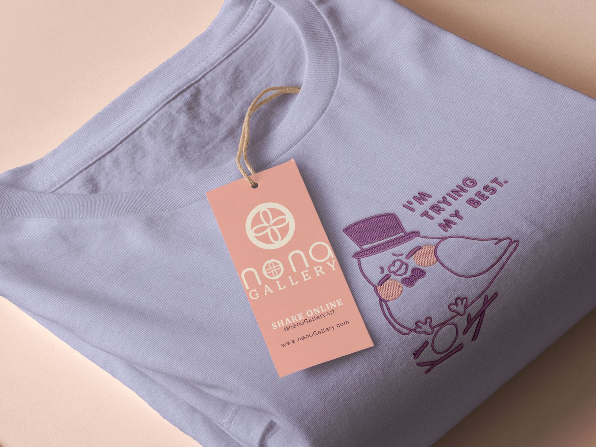An embroidered purple t-shirt design of a cute pigeon wearing a top hat building a pathetic nest and the text I'm trying my best.