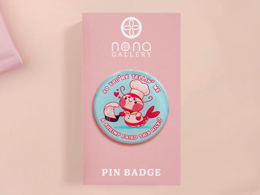 A clear acrylic pin badge with a pink heart-shaped pin back clasp. The design of the pin badge is of a cute chibi shrimp in a chefs outfit cooking with the quote So you're telling me a shrimp fried this rice?