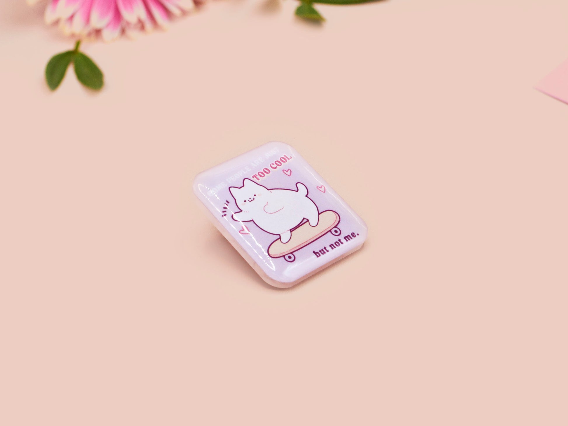 Clear acrylic pin badge with a pink heart-shaped rubber pin back clasp. The design of the pin badge is a cute chibi white cat skateboarding with the quote some people are just too cool but not me.