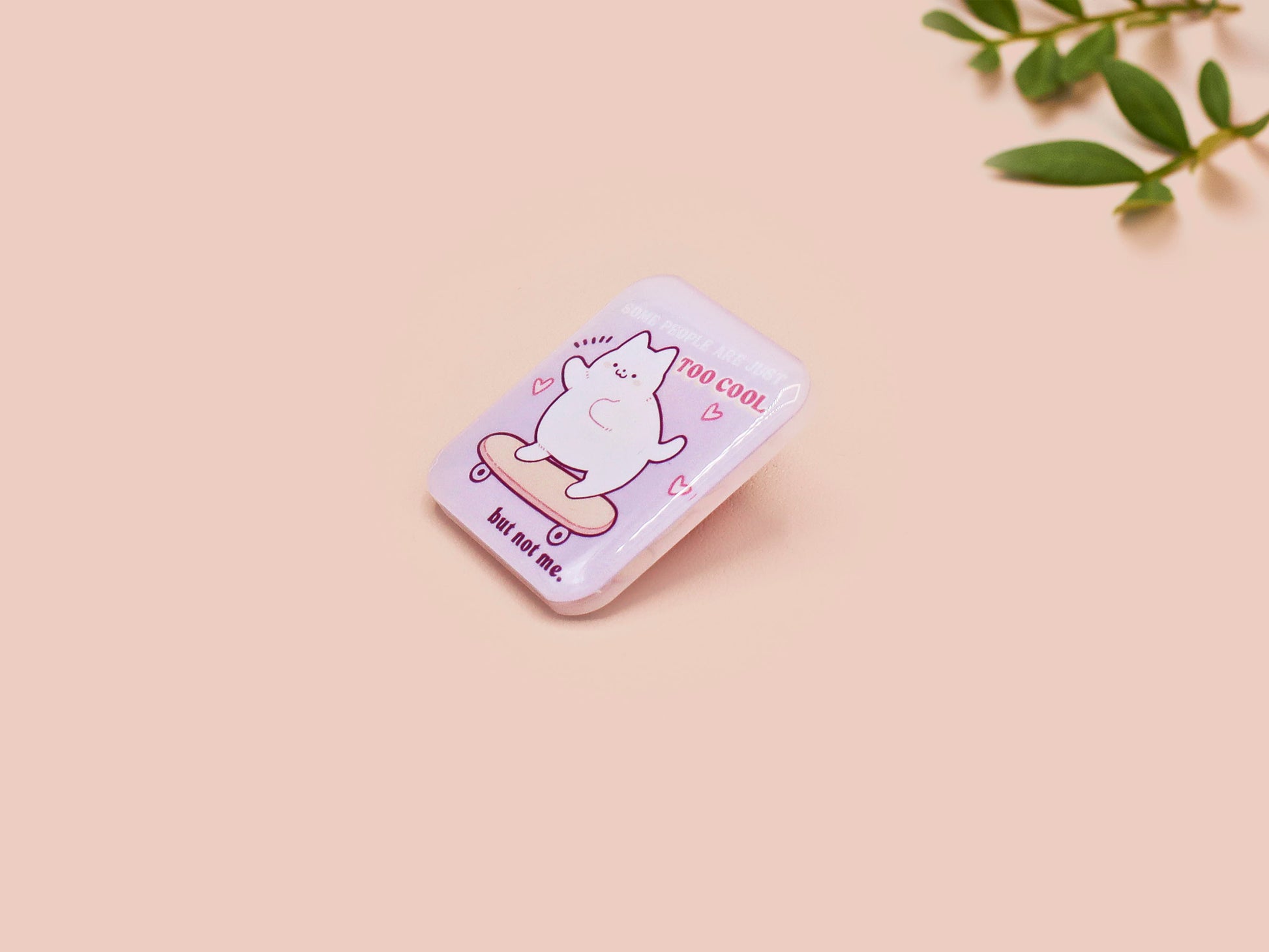 Clear acrylic pin badge with a pink heart-shaped rubber pin back clasp. The design of the pin badge is a cute chibi white cat skateboarding with the quote some people are just too cool but not me.
