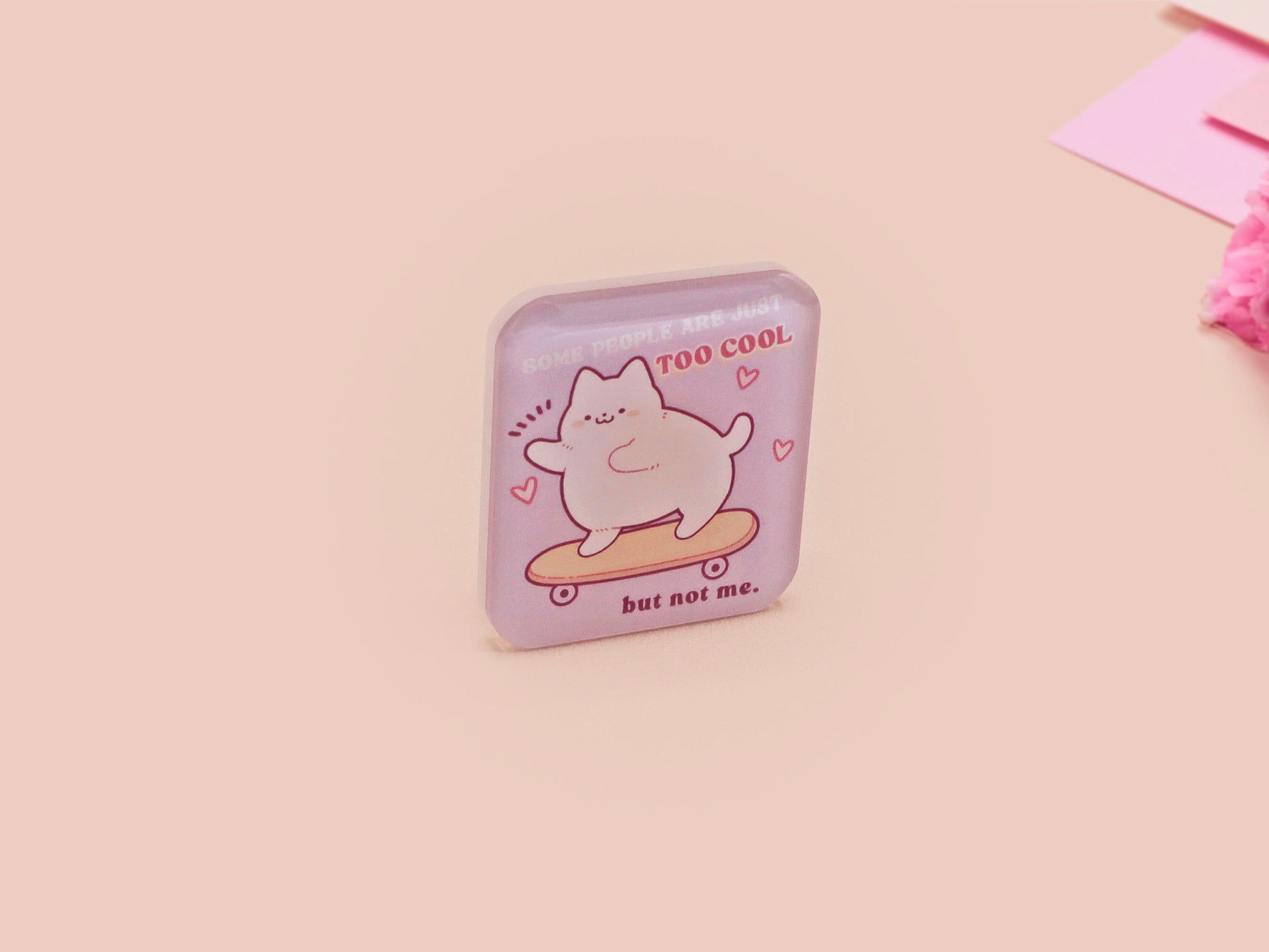 Clear acrylic pin badge with a pink heart-shaped rubber pin back clasp. The design of the pin badge is a cute chibi white cat skateboarding with the quote some people are just too cool but not me.