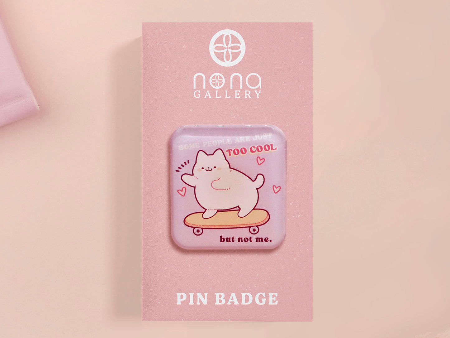 Clear acrylic pin badge with a pink heart-shaped rubber pin back clasp. The design of the pin badge is a cute chibi white cat skateboarding with the quote some people are just too cool but not me.