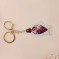 A large transparent acrylic shaker keychain with gold keyring, shaped like a traditional cute chibi soy sauce fish bottle and filled with liquid black gliter and confetti 