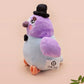 An adorable purple and blue pigeon bird plushie toy with cute embroidered eyes and facial expression, wearing a black top hat and bow tie, with a hang tag describing the pigeon as Susan.