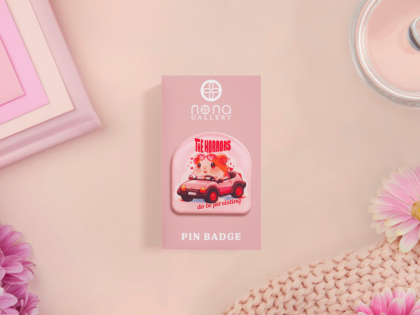 Clear acrylic pin badge with a pink heart-shaped rubber pin back clasp. The design of the pin badge is a cute chibi guinea pig hamster driving a pink car and the quote the horrors do be persisting.