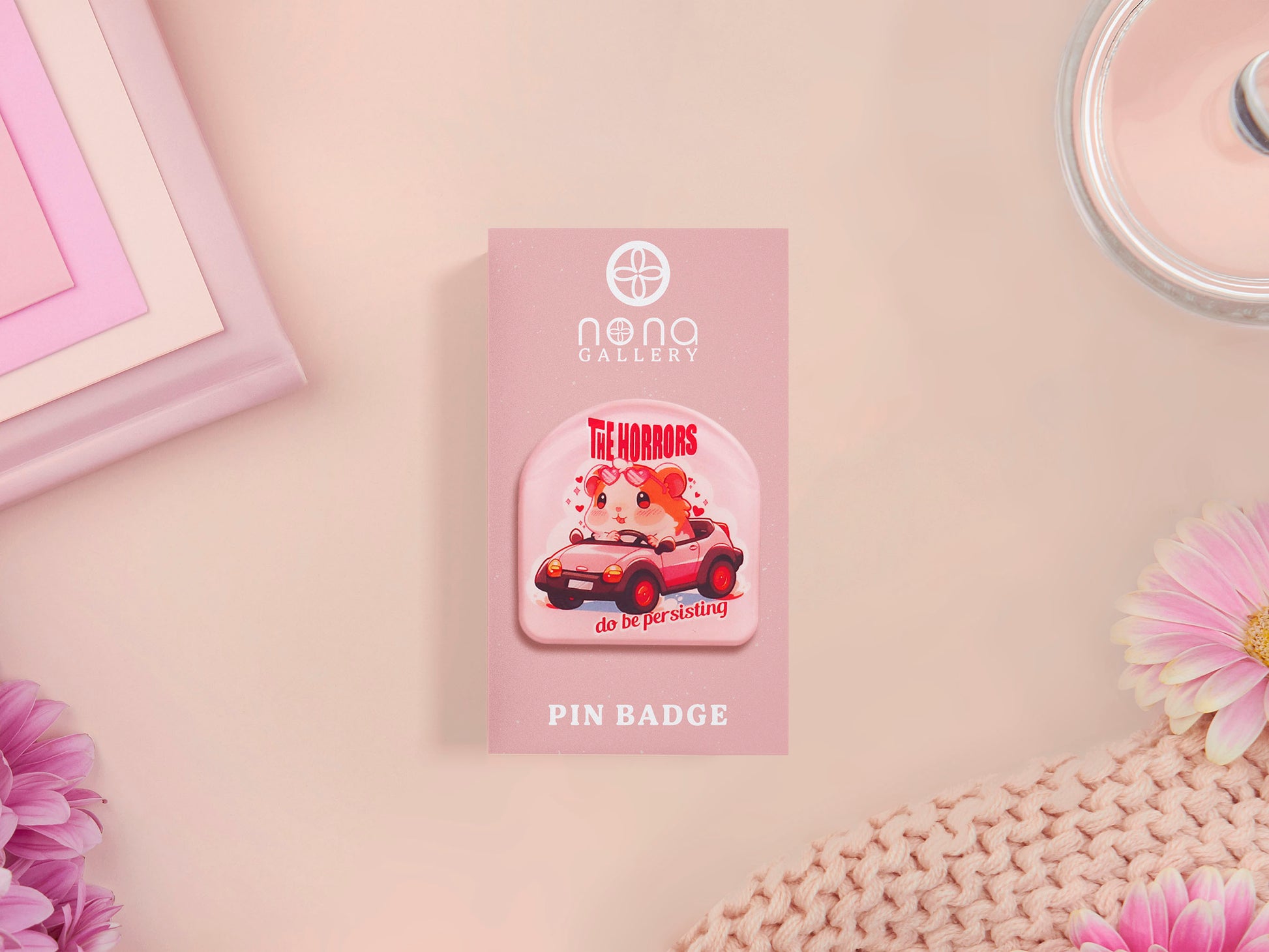 Clear acrylic pin badge with a pink heart-shaped rubber pin back clasp. The design of the pin badge is a cute chibi guinea pig hamster driving a pink car and the quote the horrors do be persisting.