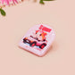 Clear acrylic pin badge with a pink heart-shaped rubber pin back clasp. The design of the pin badge is a cute chibi guinea pig hamster driving a pink car and the quote the horrors do be persisting.