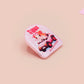 Clear acrylic pin badge with a pink heart-shaped rubber pin back clasp. The design of the pin badge is a cute chibi guinea pig hamster driving a pink car and the quote the horrors do be persisting.