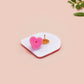 Clear acrylic pin badge with a pink heart-shaped rubber pin back clasp. The design of the pin badge is a cute chibi guinea pig hamster driving a pink car and the quote the horrors do be persisting.