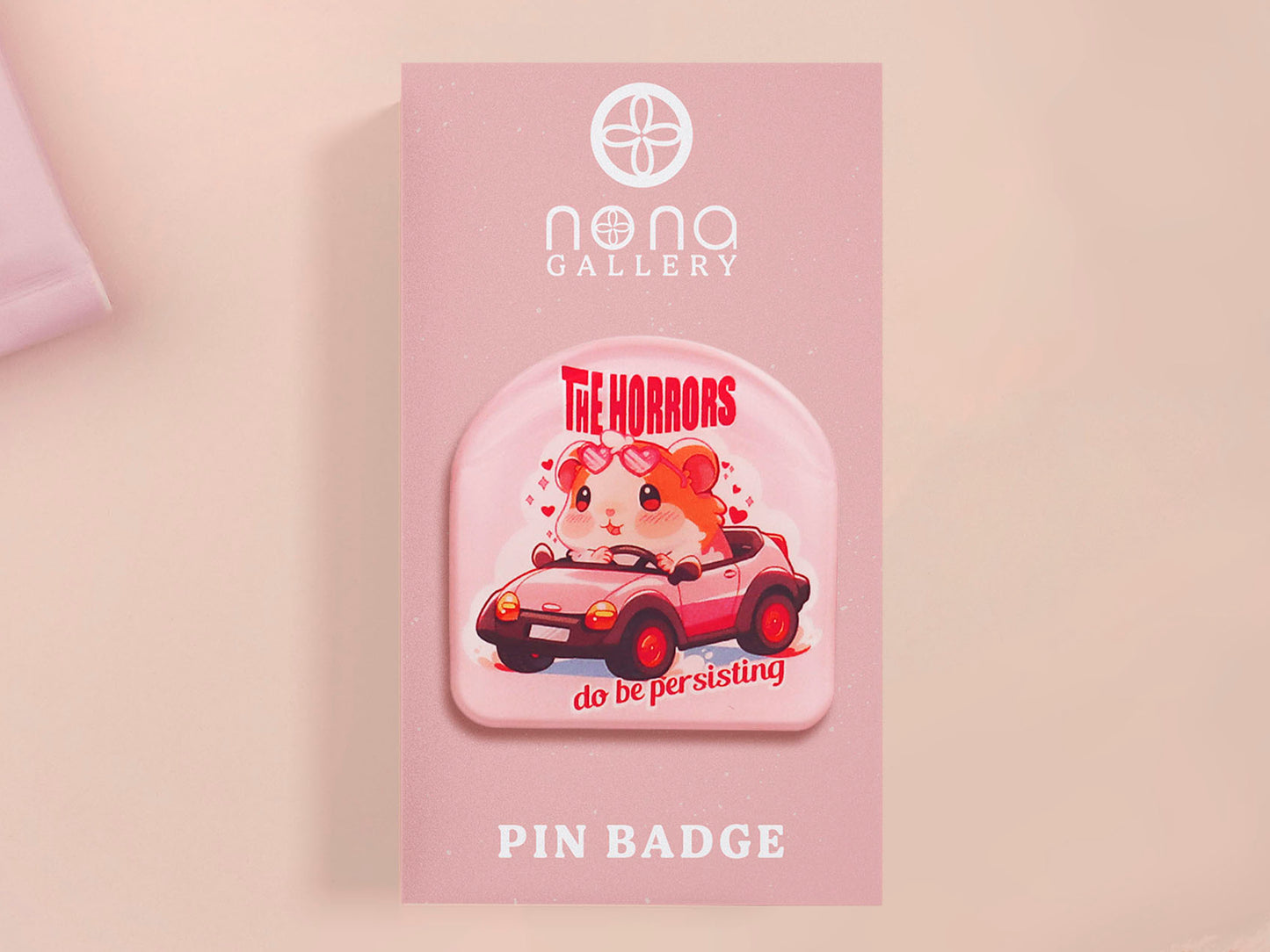 Clear acrylic pin badge with a pink heart-shaped rubber pin back clasp. The design of the pin badge is a cute chibi guinea pig hamster driving a pink car and the quote the horrors do be persisting.
