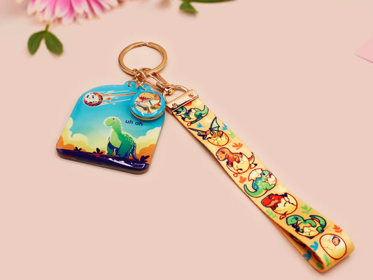 Acrylic epoxy dinosaur keychain with a large acrylic charm of a long necked dinosaur looking up at an incoming asteroid with the quote uh oh, a smaller charm of a cute trex with arm grabbers and a matching hatching baby dinosaur lanyard.