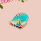 A clear acrylic pin badge with a pink heart-shaped pin back clasp. The design of the pin badge is of a cute long neck dinosur looking at an incoming asteroid with the quote uh oh.