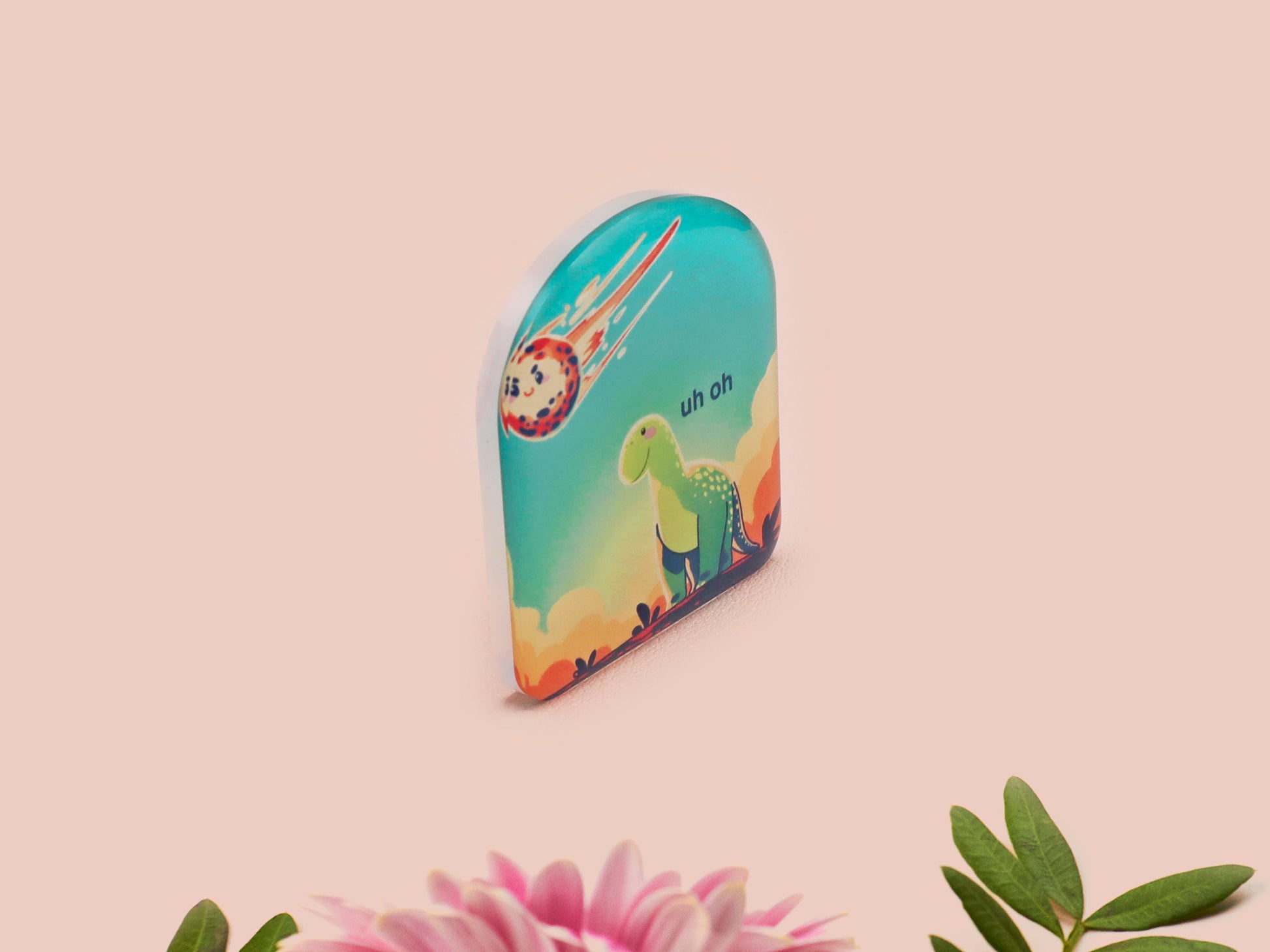 A clear acrylic pin badge with a pink heart-shaped pin back clasp. The design of the pin badge is of a cute long neck dinosur looking at an incoming asteroid with the quote uh oh.