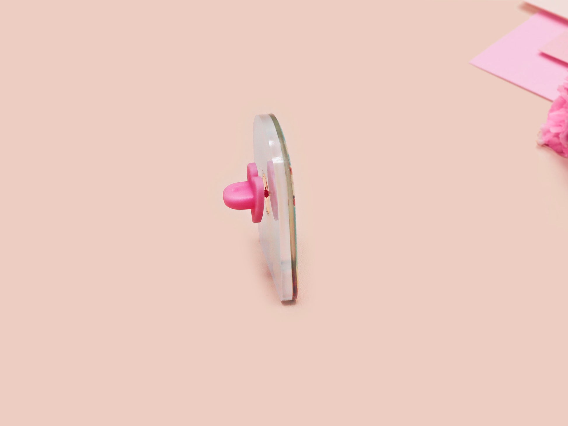 A clear acrylic pin badge with a pink heart-shaped pin back clasp. The design of the pin badge is of a cute long neck dinosur looking at an incoming asteroid with the quote uh oh.