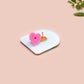A clear acrylic pin badge with a pink heart-shaped pin back clasp. The design of the pin badge is of a cute long neck dinosur looking at an incoming asteroid with the quote uh oh.
