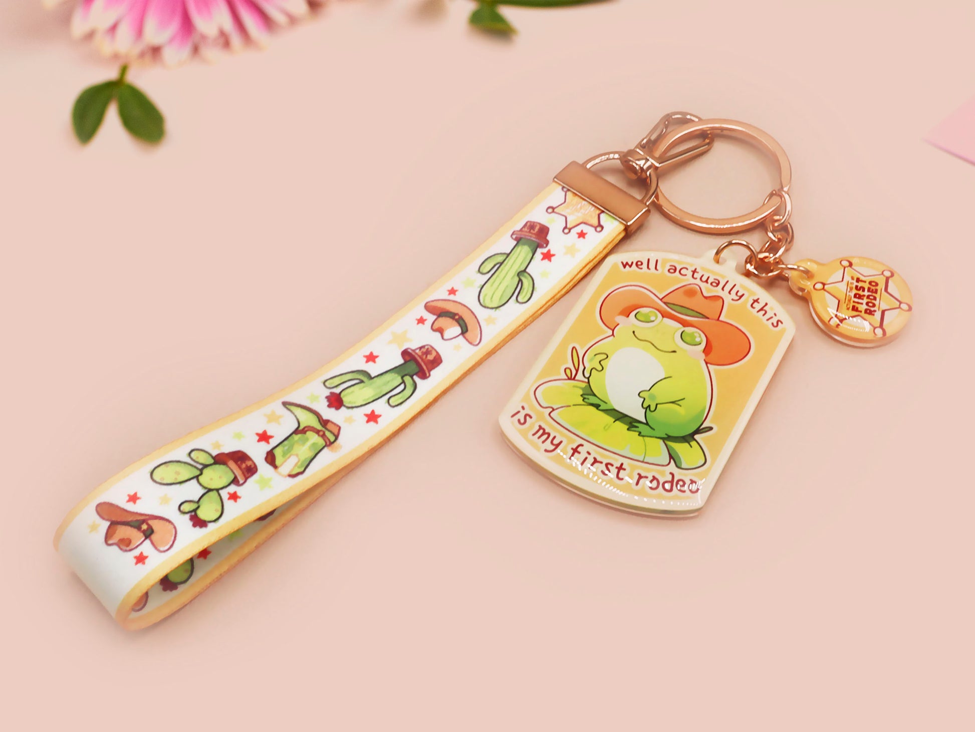 Acrylic keychain and lanyard of a cute cowboy frog with the quote well actually this is my first rodeo With a matching mini sherrif badge charm and lanyard of different country western items like cactus, stetsons and cowboy boots.