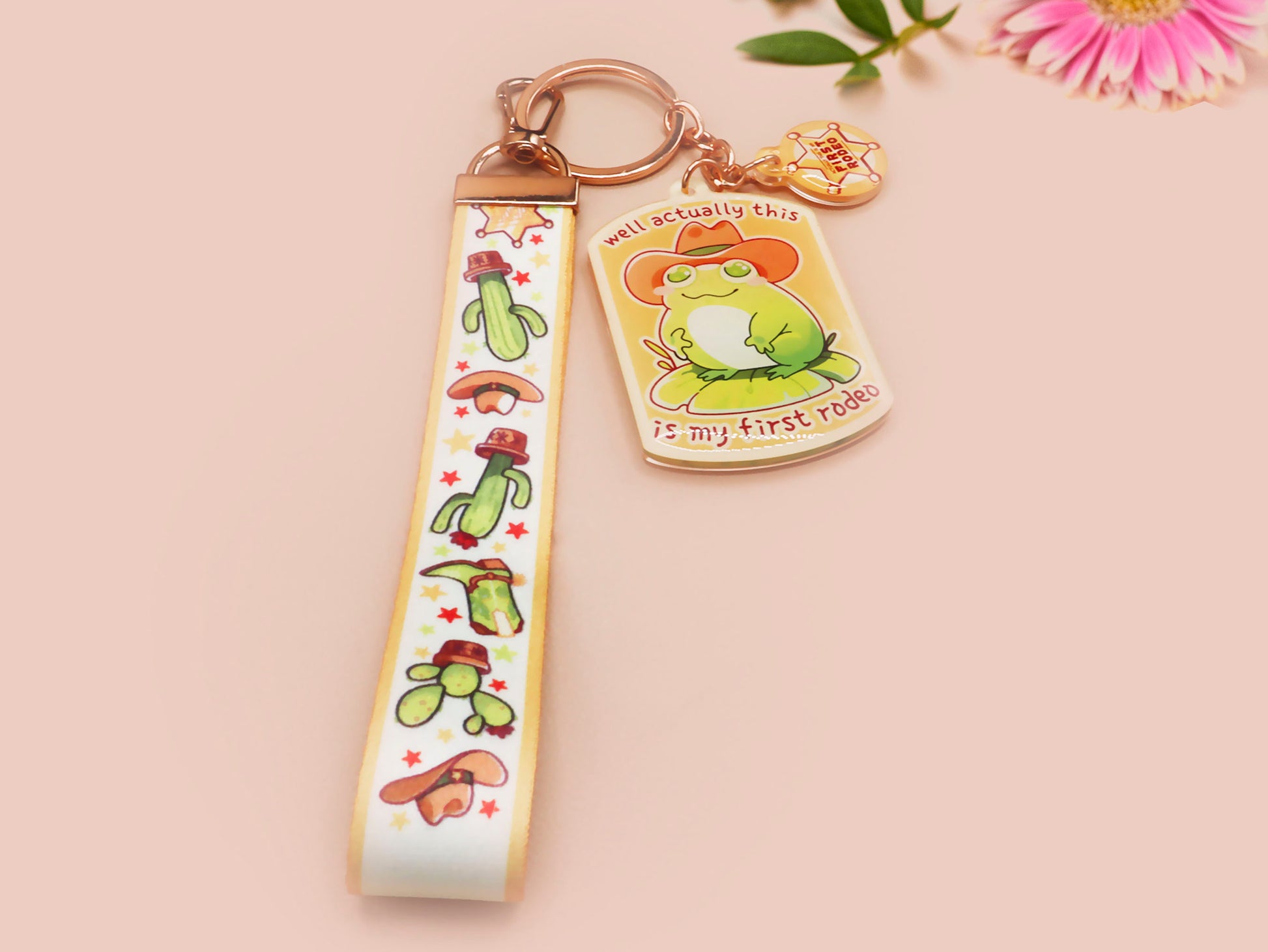 Acrylic keychain and lanyard of a cute cowboy frog with the quote well actually this is my first rodeo With a matching mini sherrif badge charm and lanyard of different country western items like cactus, stetsons and cowboy boots.