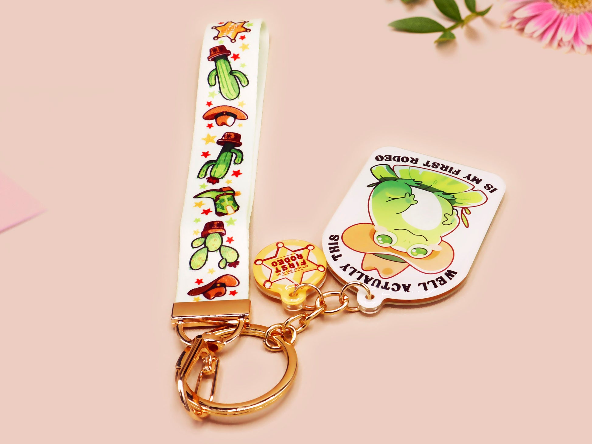 Acrylic epoxy cowboy frog keychain with a large acrylic charm of a cute cowboy frog wearing a stetson hat with the quote well actually this is my first rodeo, a smaller charm of a cute sherrifs badge and a matching cactus and cowboy boots and hats lanyard.